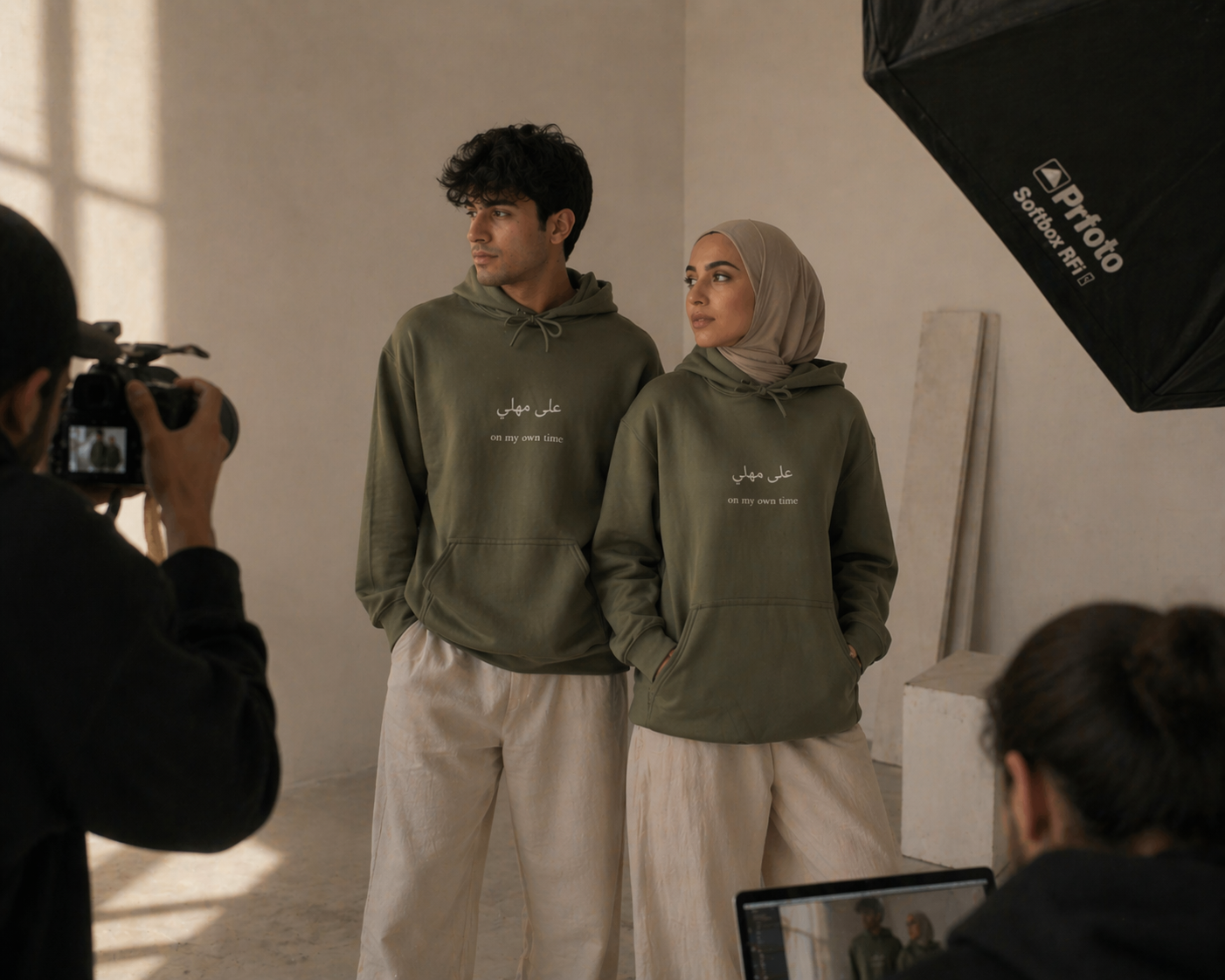 Two people wearing green hoodies with text, standing in a studio setting with photography equipment.